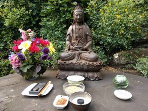 Kuan Yin garden altar, with candles, flowers, water, incense, and a Japanese ink brush.