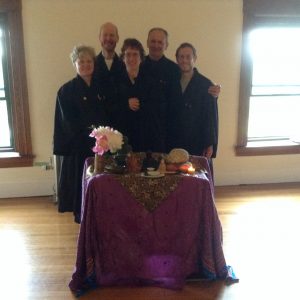 Five smiling Zen practitioners are arranged behind an altar with various Buddha images.