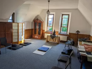 Inviting view of a Zendo with altar, black cushions and chairs for sitting, and a computer for online connections.